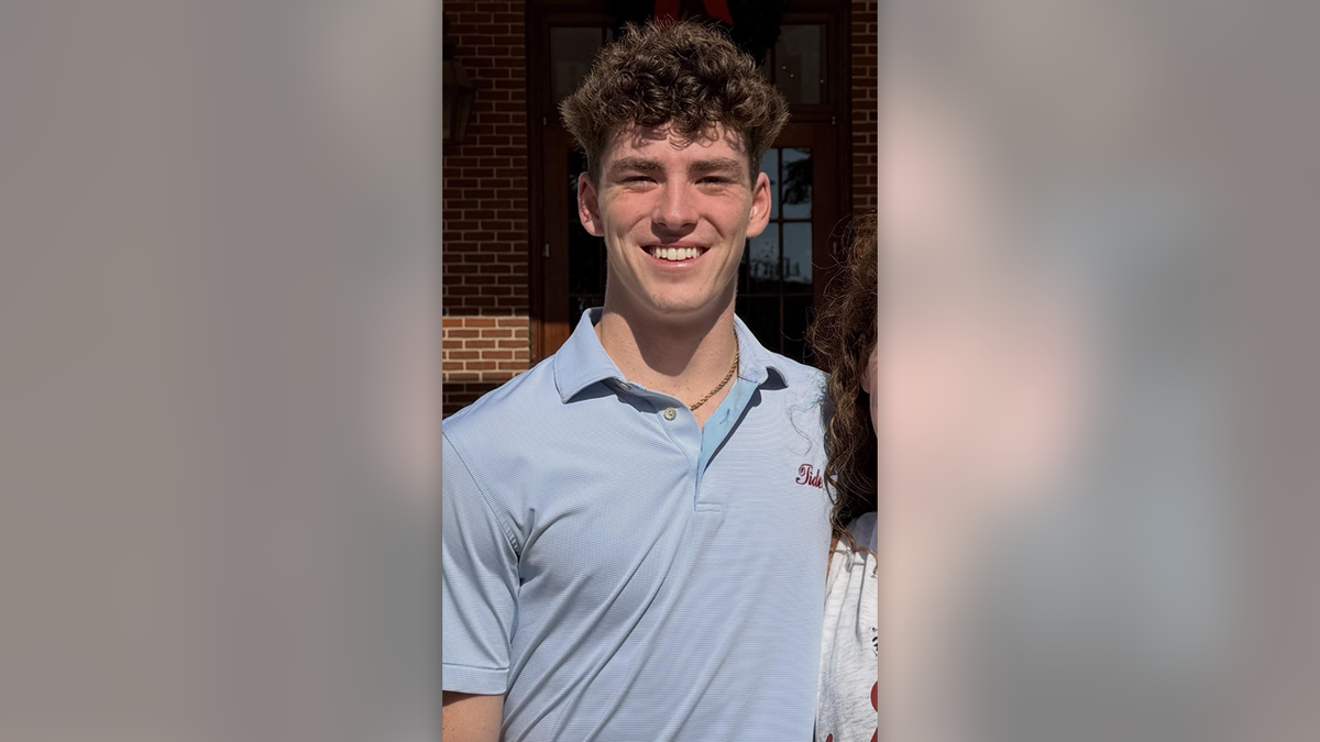 Jimmy Gracey has curly brown hair as he smiles wearing a light blue Alabama golf shirt