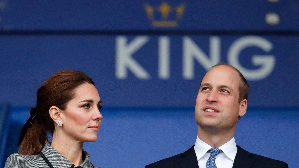 Kate Middleton looking at Prince William with the King logo above his head.