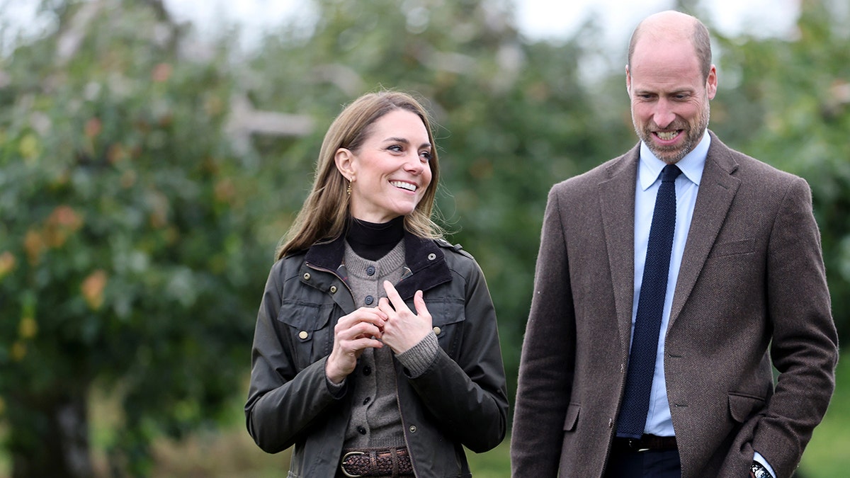 Prince William and Kate Middleton walking together as she smiles adoringly at him.