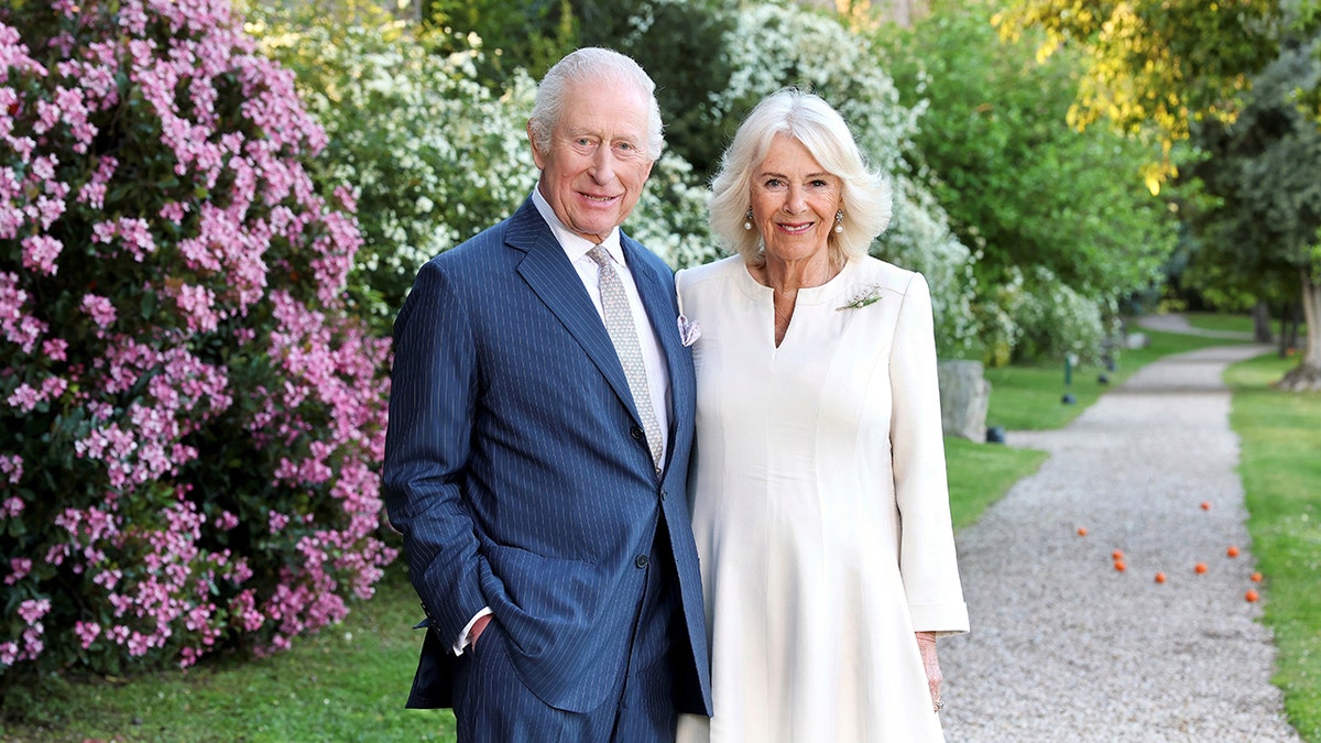 King Charles and Queen Camilla posing together for a portrait in front of flowers.