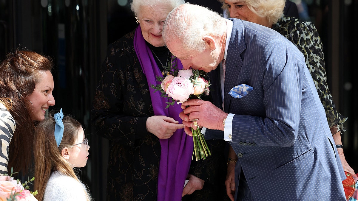 King Charles smelling flowers handed to him by a little girl.