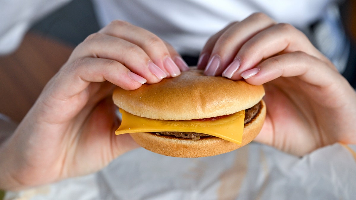 A woman's hands hold a McDonald's cheeseburger in an arch shape.