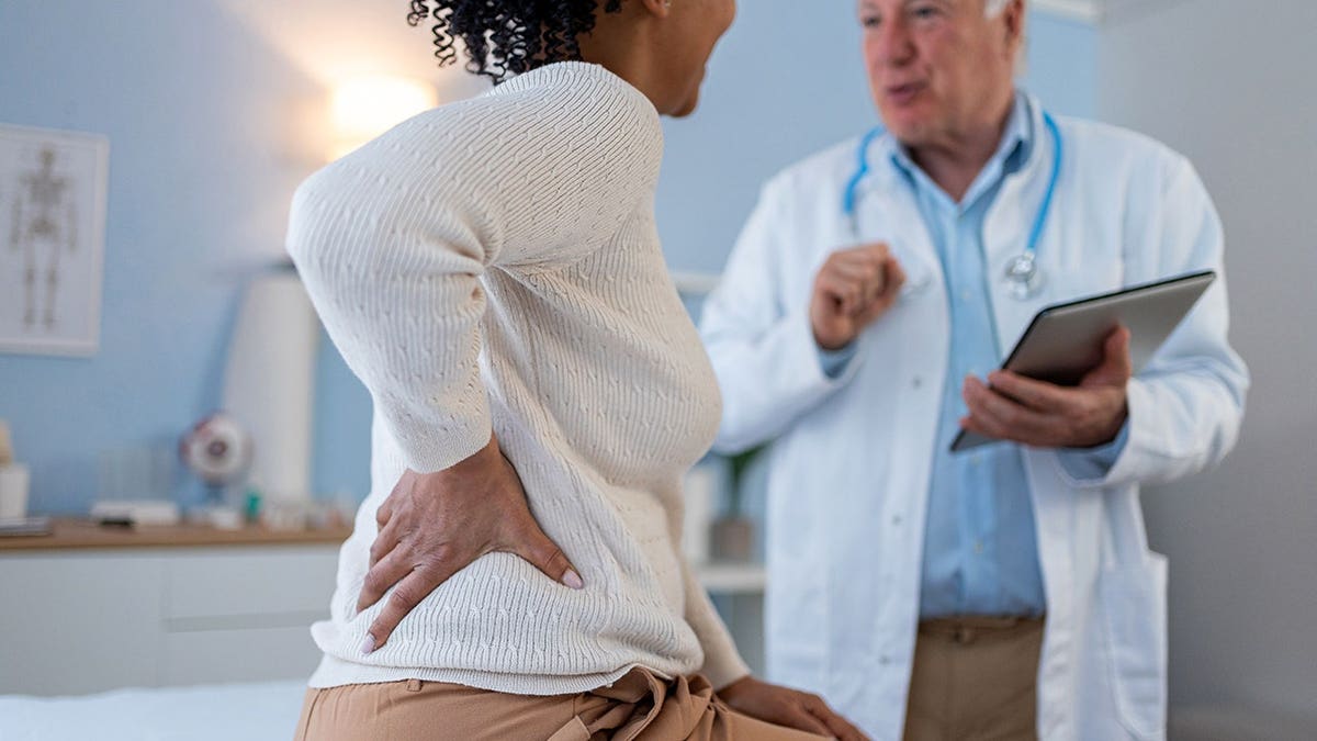 An older Caucasian male doctor examining a middle-aged African-American female patient in a doctor's office.