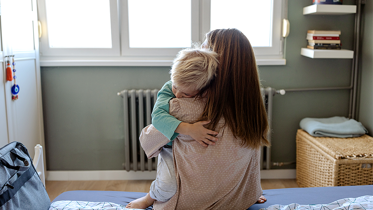 Mother holding baby, back view sitting on bed