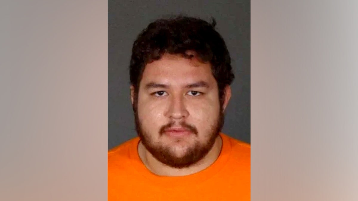Omar Cardenas in a orange jumpsuit in front of a brown background