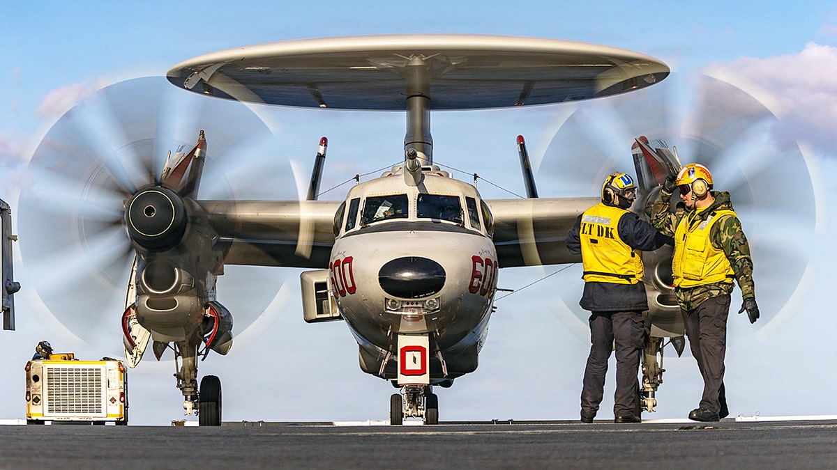 U.S. Navy Sailors signaling to an E-2D Hawkeye aircraft as it taxis on the flight deck of the USS Gerald R. Ford.