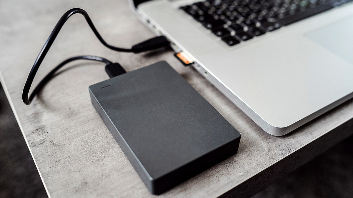 An external hard drive is plugged into a laptop with an SD card sticking out of its side.