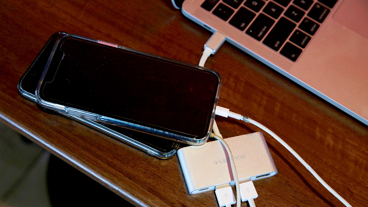 Two phones are plugged into a laptop through a splitter.
