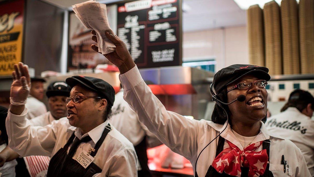 Two expeditors at Portillo's deliver over a busy counter their famous Chicago hot dogs in downtown Chicago, Illinois Friday May 15, 2015, looking happy waving tickets.