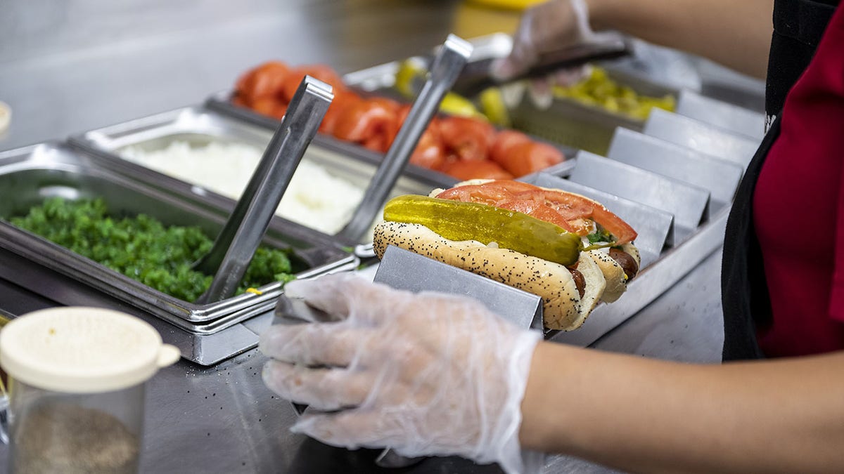 An employee prepares a hot dog at a Portillo's restaurant in Chicago, Illinois, US, on Tuesday, Sept. 27, 2022. Topping seen in background as employee loads up hot dogs.