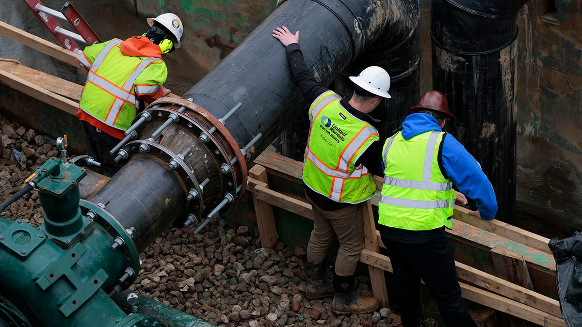 Workers look on at the C&O Canal around a broken section of the Potomac Interceptor on March 05, 2026 in Cabin John, Maryland. 