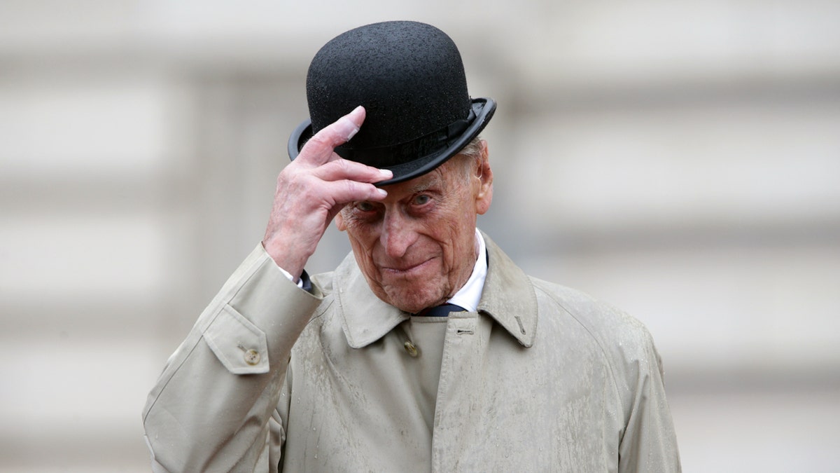 Prince Philip, Duke of Edinburgh, raising his hat while standing on a forecourt.