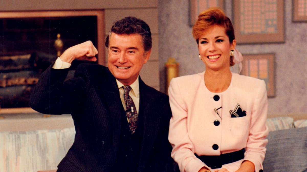 Regis Philbin and Kathie Lee Gifford smiling and sitting on a white couch in front of an audience.