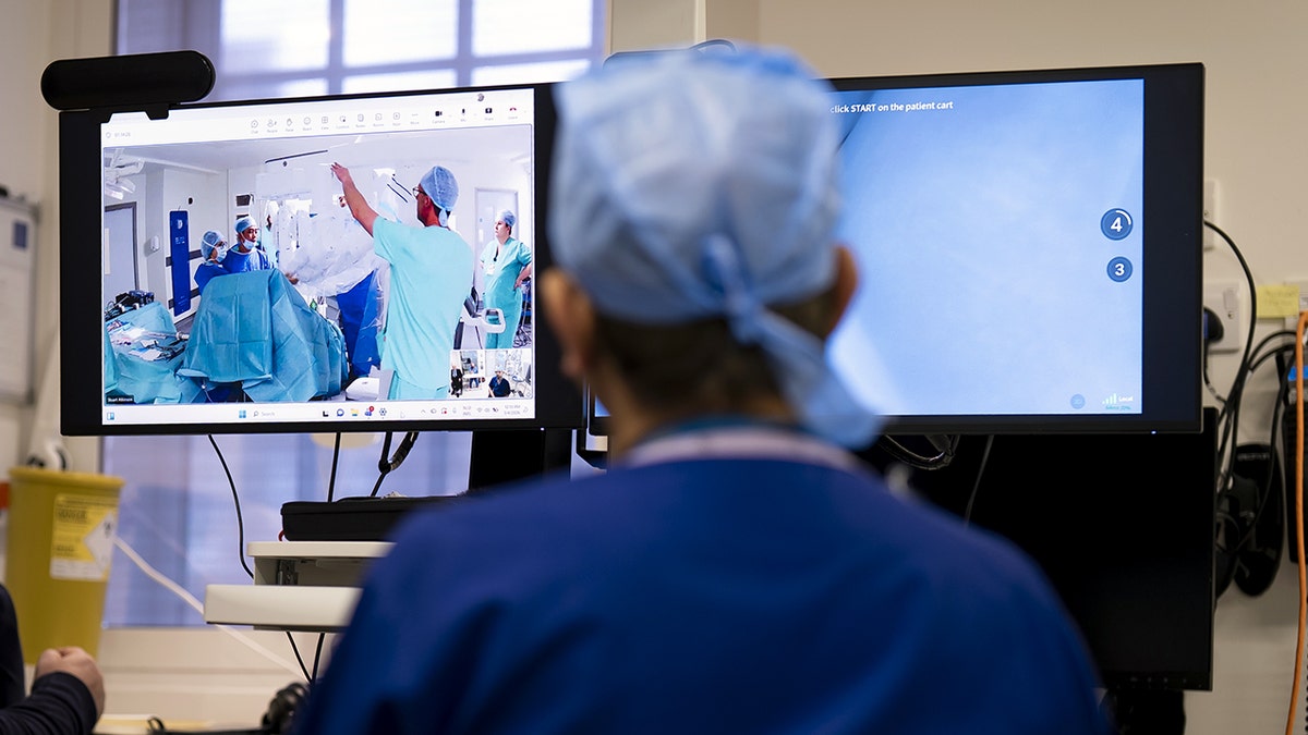 A surgeon looks at two screens showing a live feed of operating room in another country.