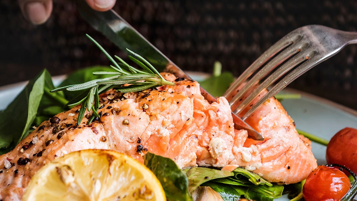Salmon on a plate is being cut with a knife and fork.