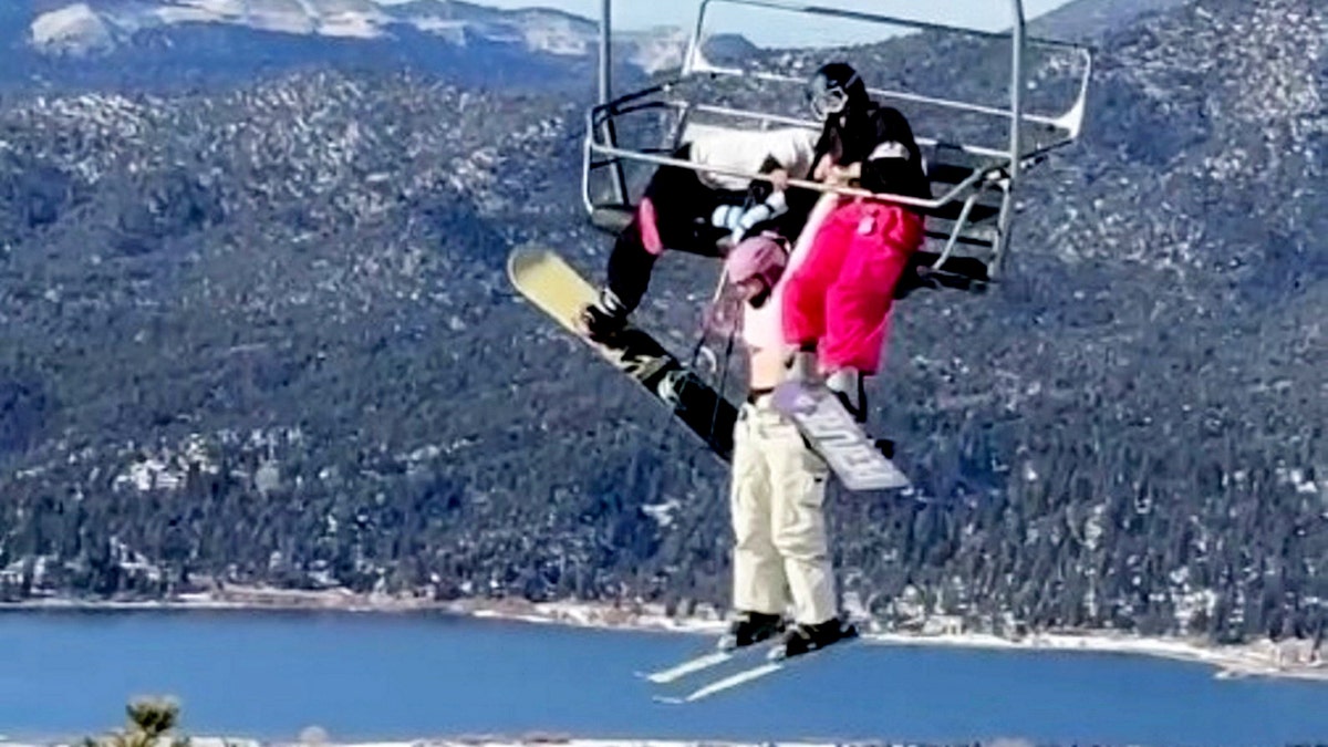 Skier dangles from chairlift in California above snowy mountain landscape and lake.