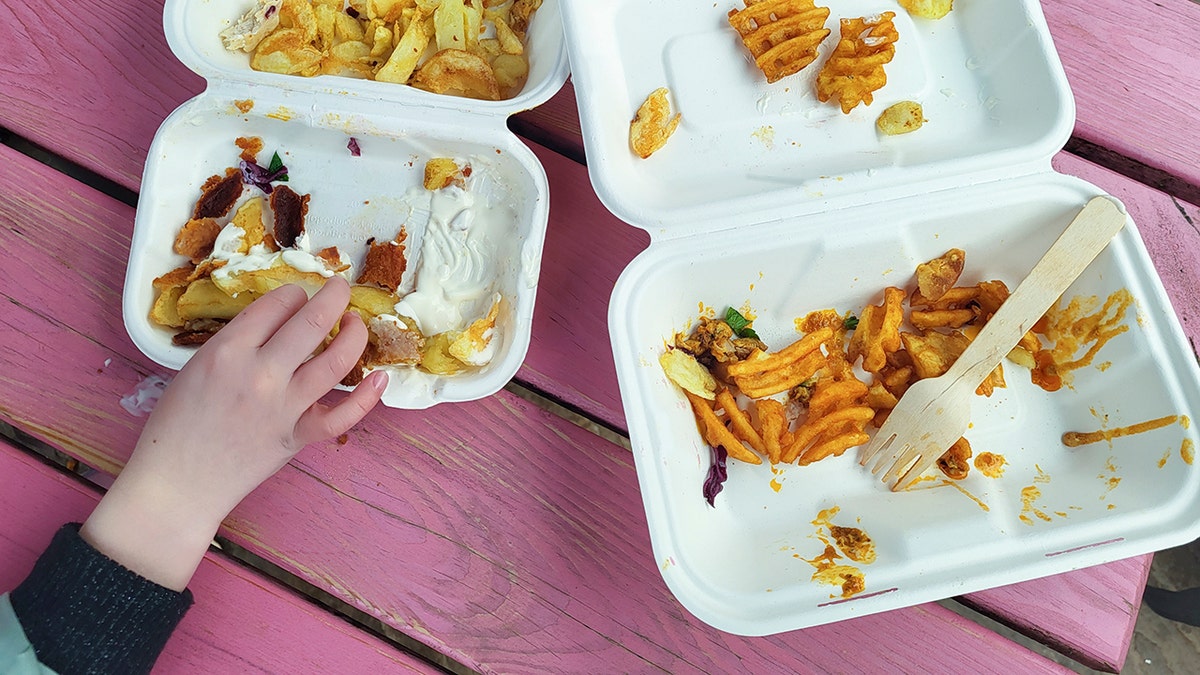 A child's hand reaches for take away food from a polystyrene lunch box.