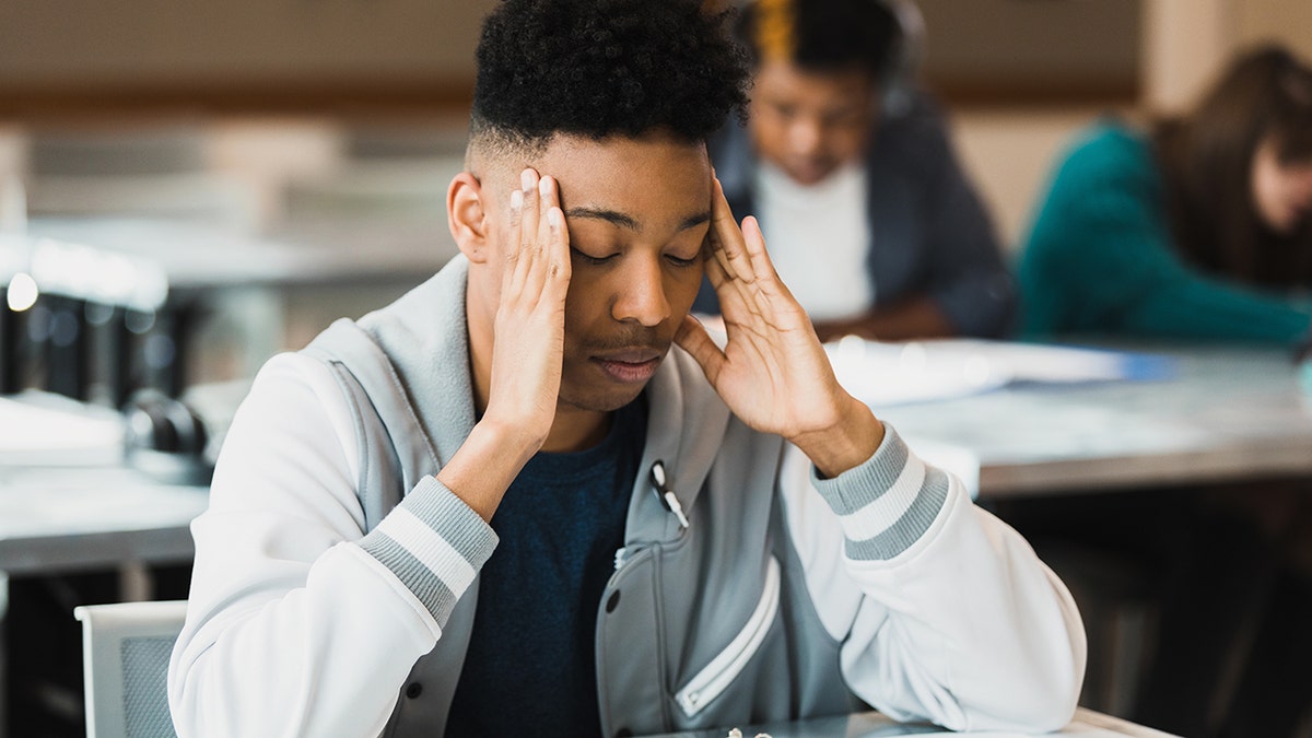 A depressed young boy has his hands on his head in sadness at school