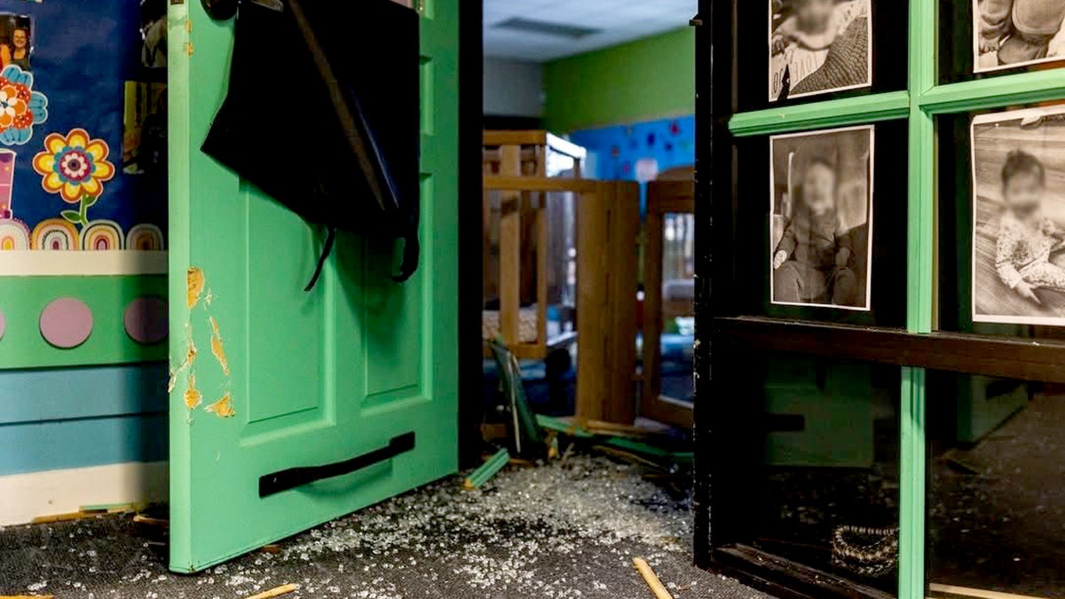 A broken door and shards of glass on the floor of the childcare center.