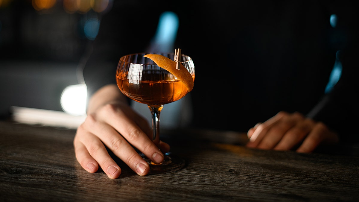 Bartender holds cocktail with orange peel as garnish.