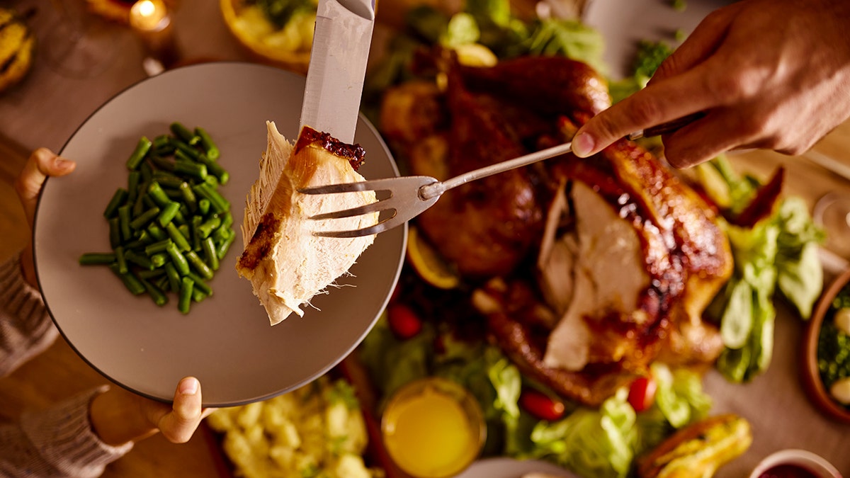 A slice of turkey is placed on a plate with green beans already on it at the dinner table.