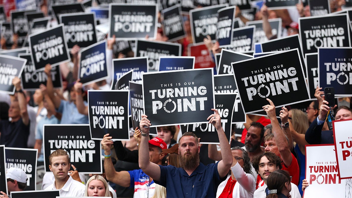 Attendees hold Turning Point USA signs at Charlie Kirk memorial.