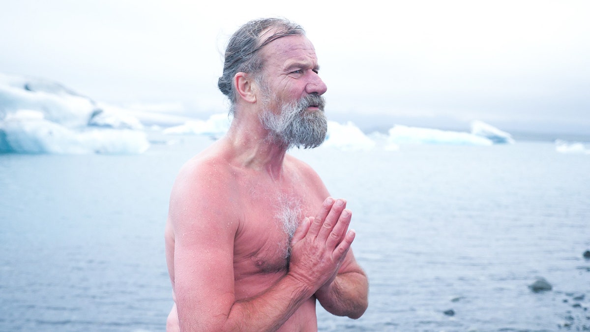 wim hof stands on icy beach in iceland with prayer hands
