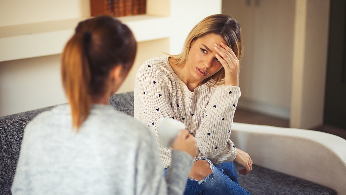 woman places hand on head while talking with a friend