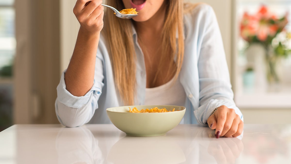 Beautiful young woman having breakfast eating cereals at home. Healthy concept.
