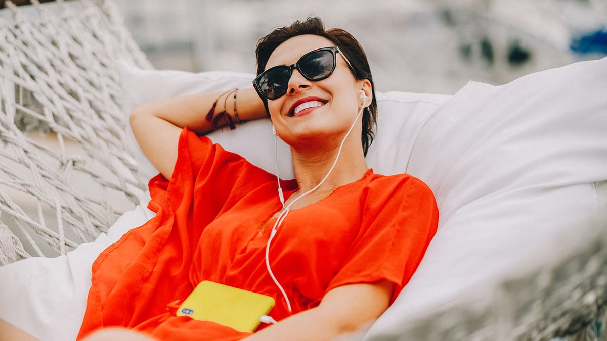 Woman at beach holiday resting in hammock and listening to music