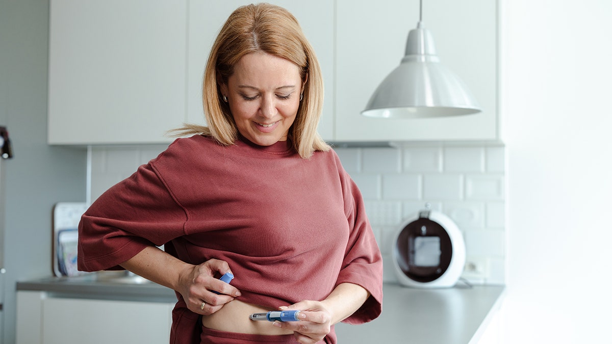 A mature woman performs a self-administered medical procedure in a home kitchen environment