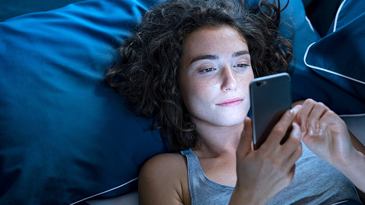 woman scrolling on phone in bed