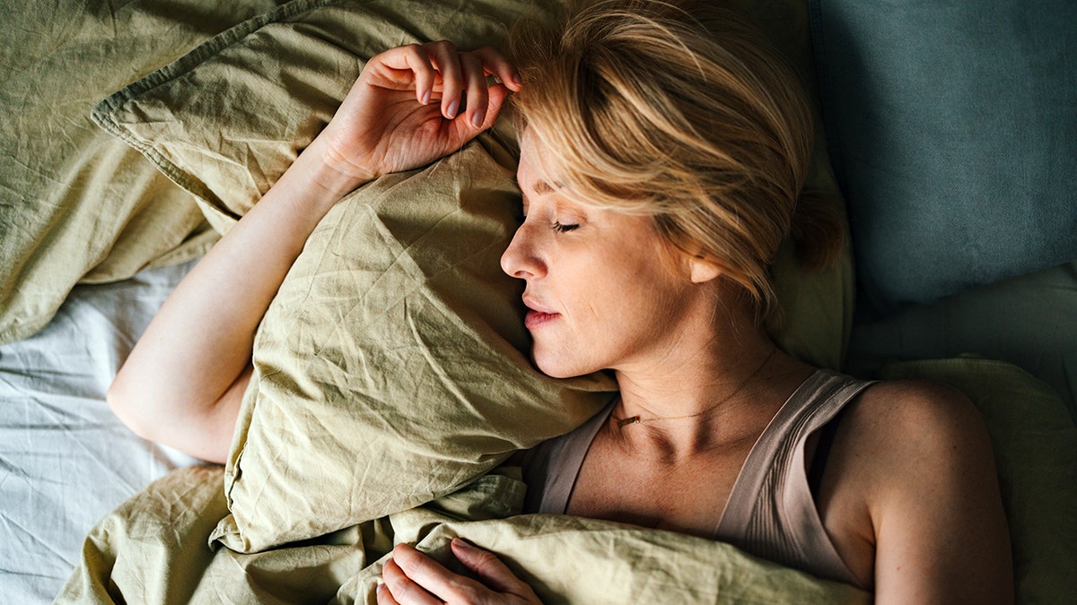 Middle-aged woman sleeping peacefully on her side in bed, resting on a green pillow.
