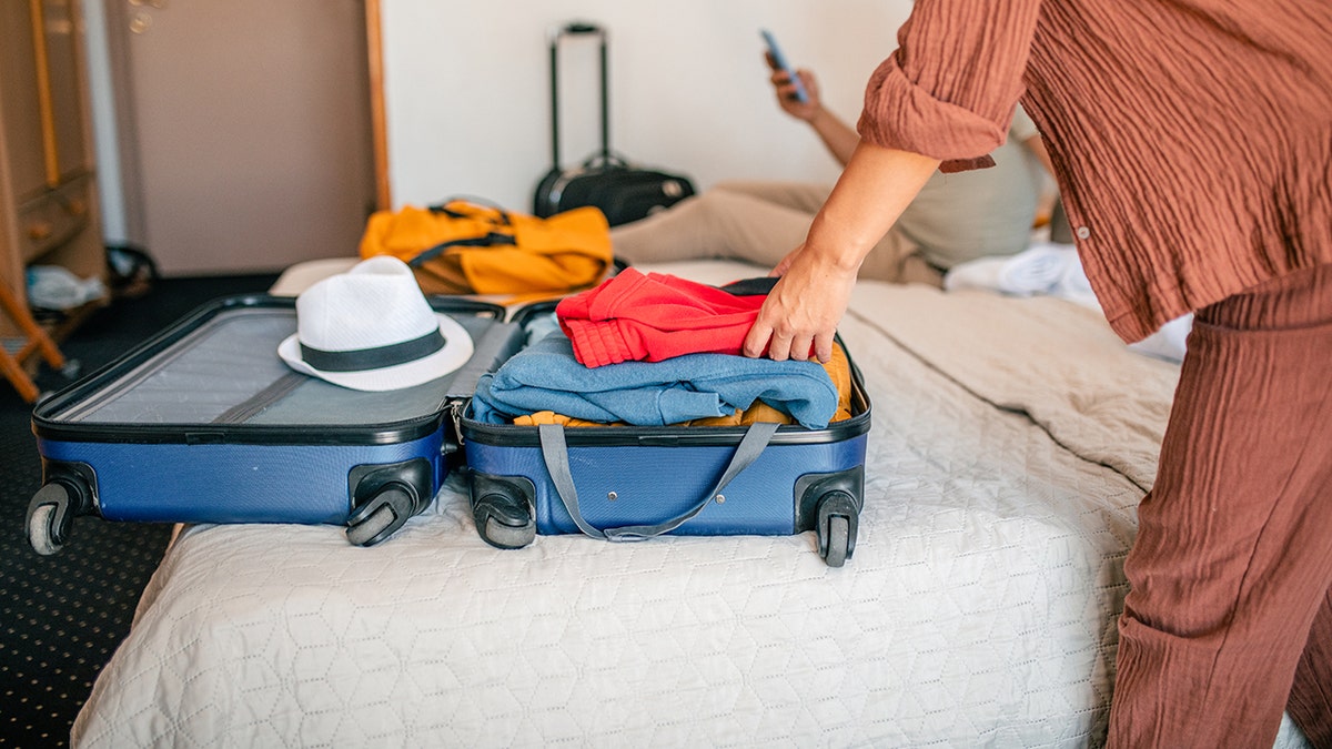 Traveler packing clothes into a suitcase on a hotel bed.