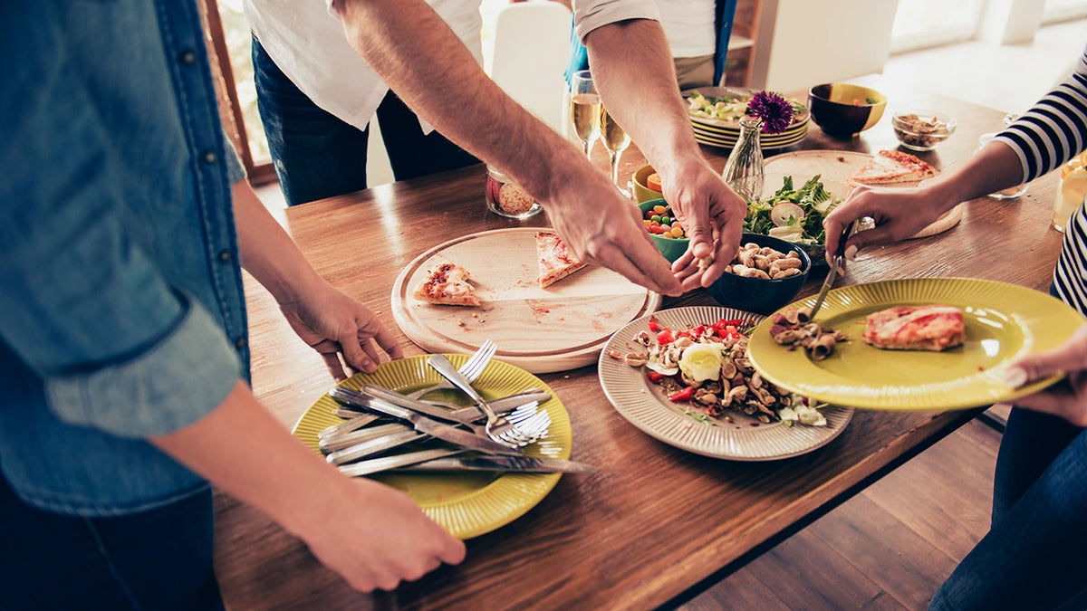 Close-up photo of people tidying the table including food, plates and silverware after a party.