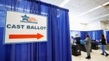A sign reading “Cast Ballot” with an arrow is seen at a Chicago early voting polling place as voters cast ballots in the background.