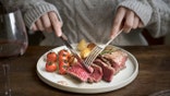 A knife and fork are used to cut into red meat on a plate.