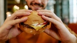 A man smiles as he holds a cheeseburger in his hands.