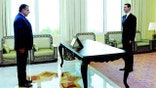 Former Syrian President Bashar al-Assad (right) standing across a desk from Samir Ousman Alsheikh in a formal room.