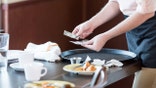 A waitress collects a cash tip while clearing a restaurant table.
