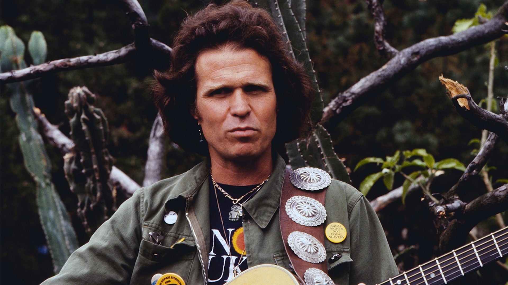 Country Joe wears green jacket and guitar