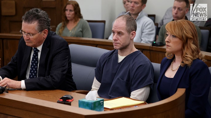 Caleb Flynn sitting at a table in a courtroom during a legal proceeding.