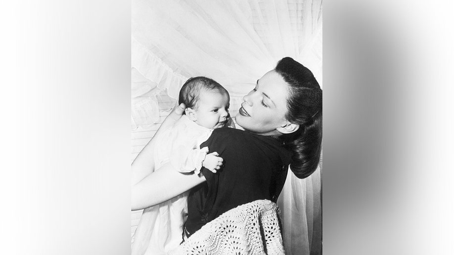 Judy Garland holding baby Liza Minnelli while looking toward the camera.