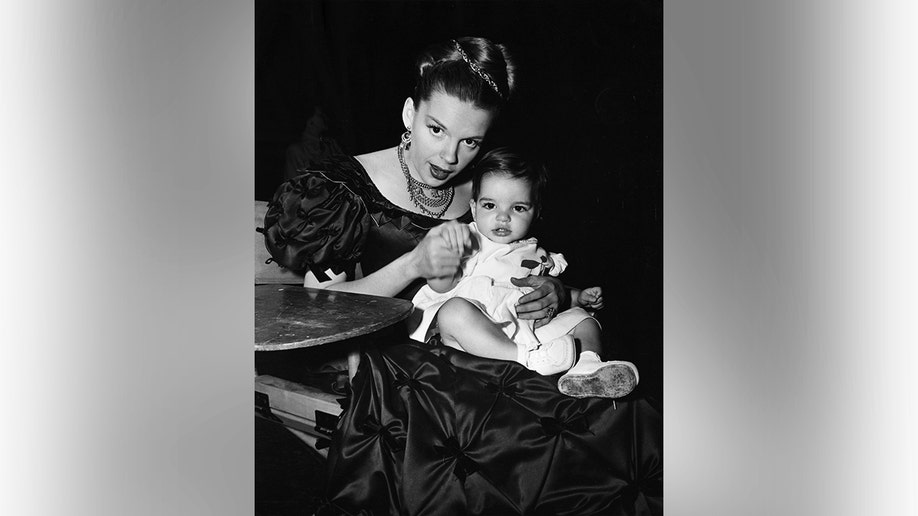Liza Minnelli and Judy Garland sitting together and looking toward the camera.