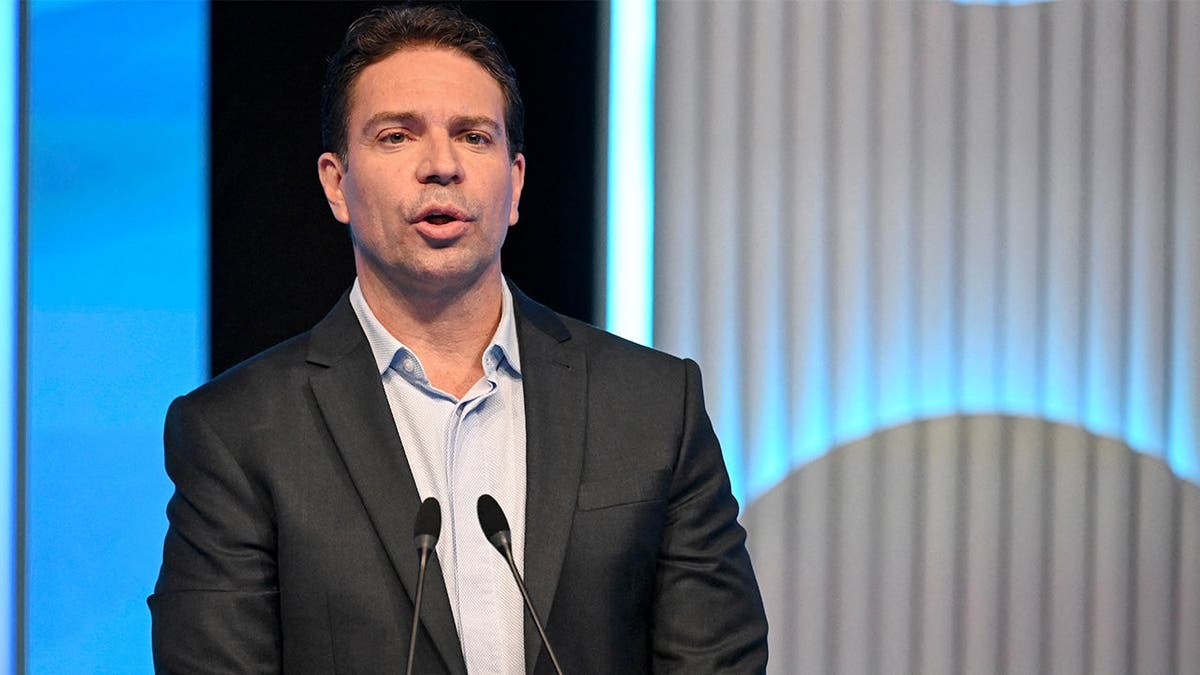 Alexandre Ramagem gesticula com as mãos em pé no pódio de um estúdio de televisão.