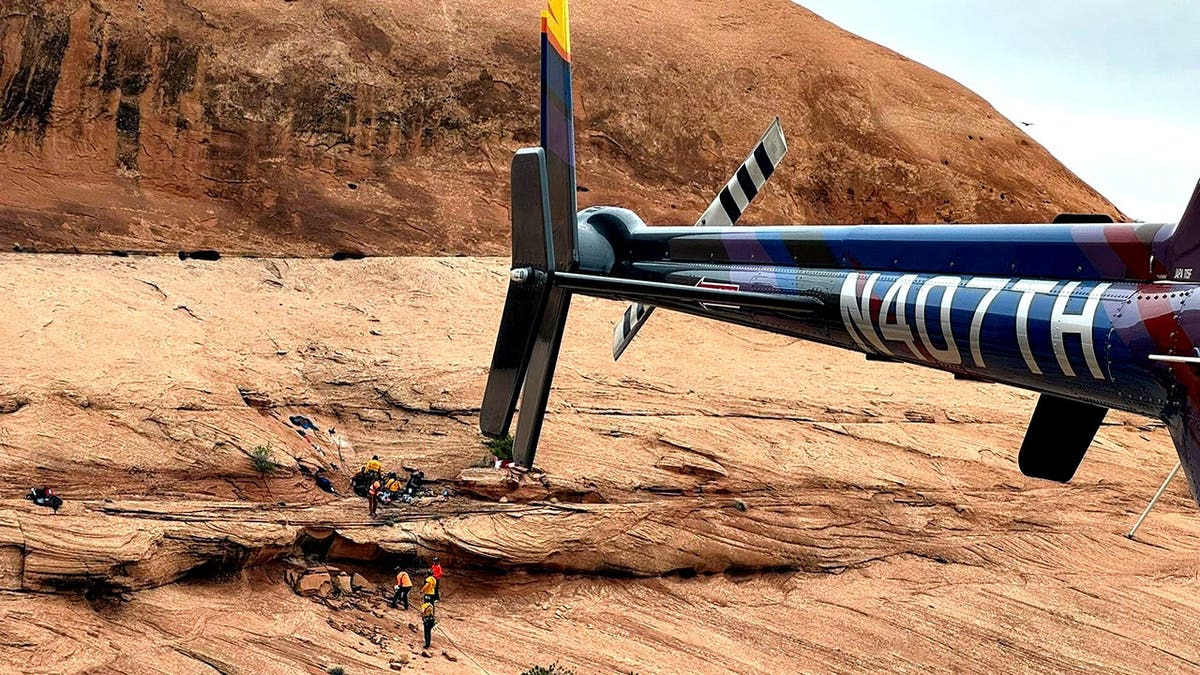 helicopter tail in foreground as rescuers work at cliff in the background