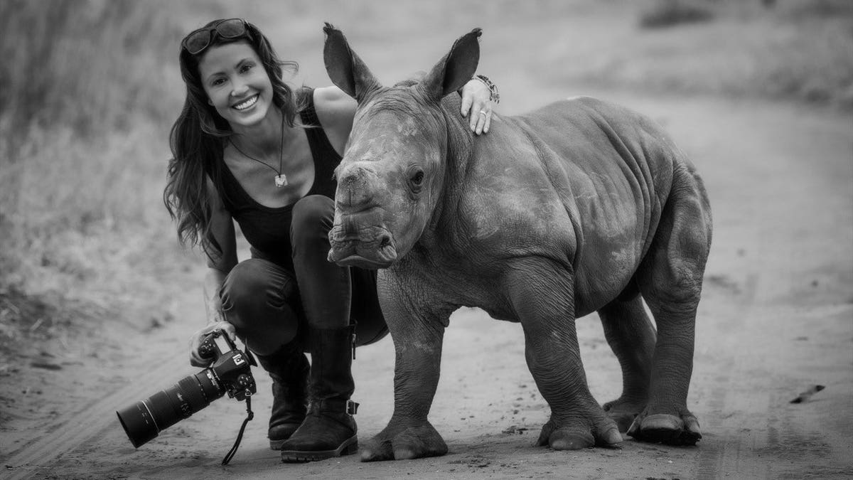 Shannon Elizabeth holding a camera and posing next to a rhino.