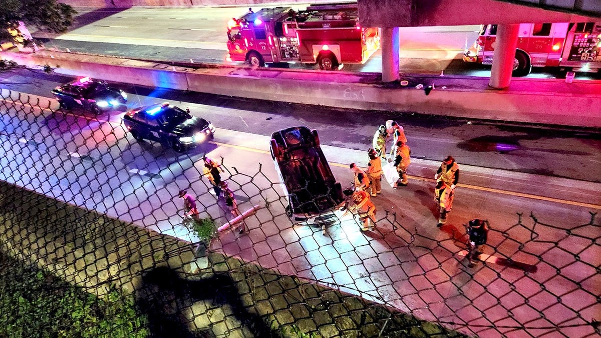 a view from the roadway bridge above the car that is overturned on the interstate