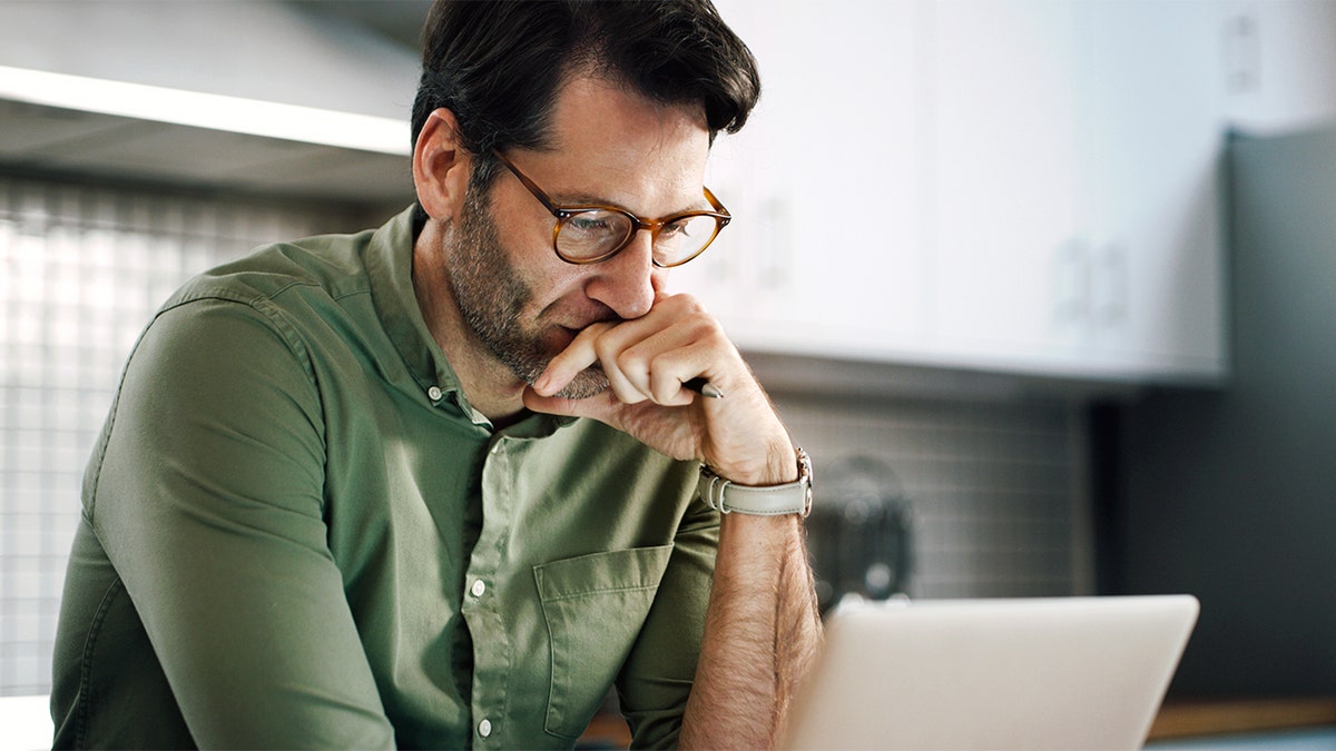 A man uses his laptop with a look of concern.