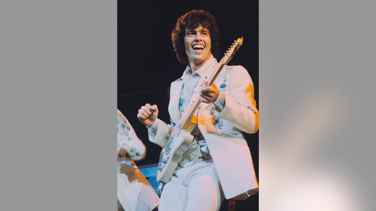 Musician Alan Osmond playing guitar on stage during a live performance